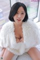 A woman in a white fur coat sitting on a bed.